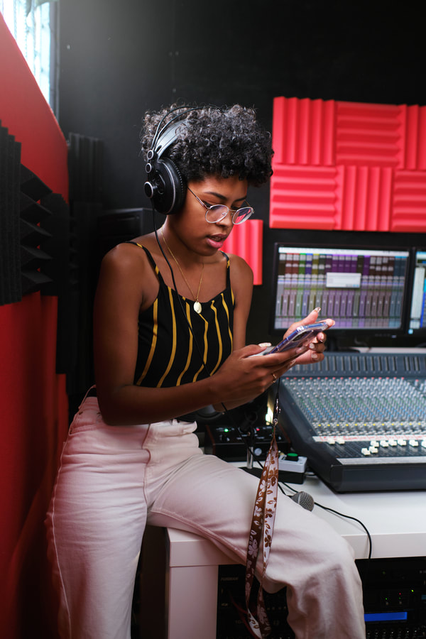 A female artist produces music with her phone in a recording studio.