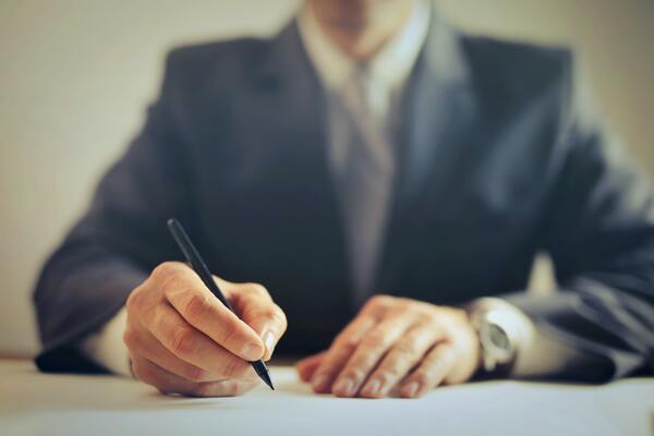Man signing important contract with pen on desk.
