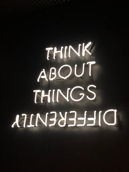 Neon sign reading 'Think About Things Differently' illuminates a dark room.