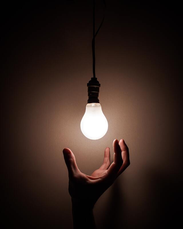 Hand reaching towards a glowing light bulb, symbolizing a brilliant idea.